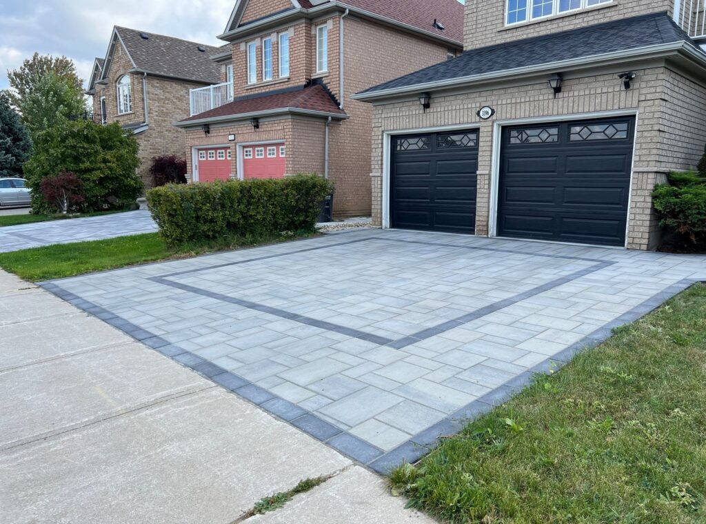 A large attached 2 car garage in front of a house with a big square interlocking paver stone driveway (Image opens in modal window)