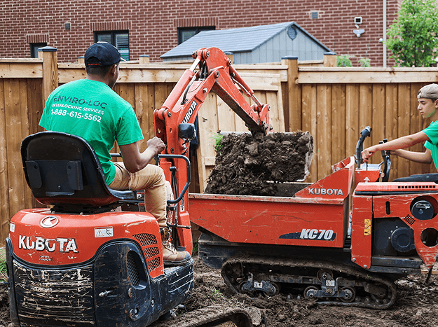 Two young men digging up a residential yard with large orange Kubota brand light construction machinery
