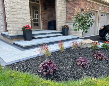 Intricate paver stone design consisting of large rectangular pavers of varying colours on a front walkway and low porch, exemplifying Interlocking paver work on a medium-sized front entrance