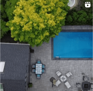 Instagram video post thumbnail showing high up aerial view of large grey paver stone patio with multiple sitting areas and tables around an in-ground pool.