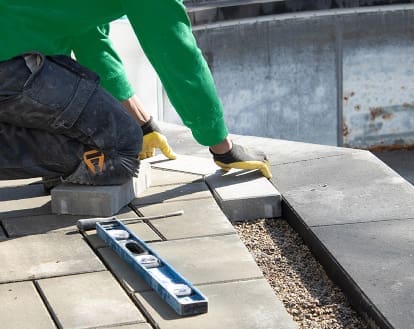 Paver patio with an individual kneeling down over top and reworking paver stones, exemplifying Interlocking Patio or Driveway Repair