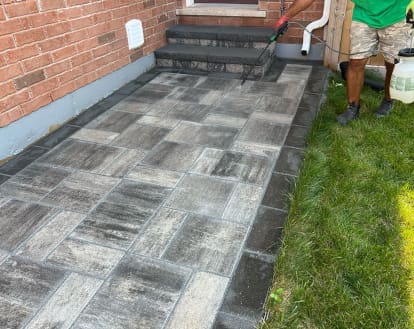 Paver walkway being sealed by an individual holding a sprayer nozzle over top, exemplifying Pressure Wash, New Polymeric Sand, and Seal services.