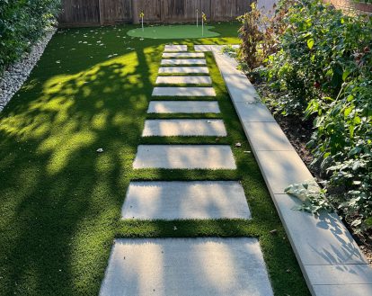 Custom golf area in residential backyard consisting of large rectangular paver stones and 3 holes surrounded by green artificial turf, exemplifying artificial turf work on a large area