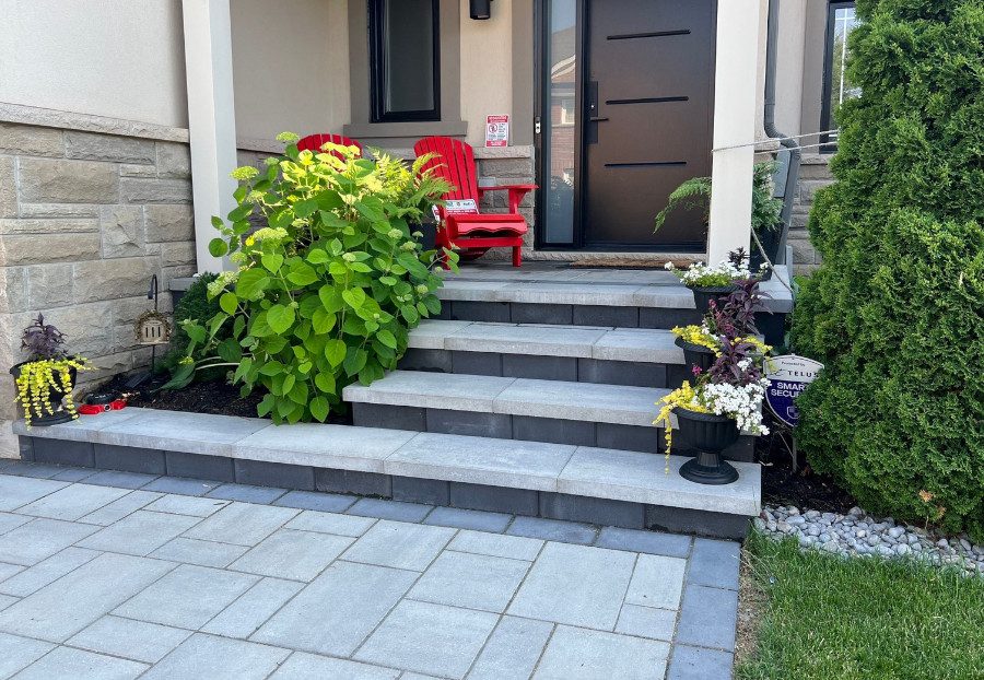 Residential property with light grey paver stone front porch, 4 light grey paver stone steps, and a paver stone walkway leading up to it. All paver stones are a light grey except for the stair risers and perimeter of the walkway, which are a darker grey.