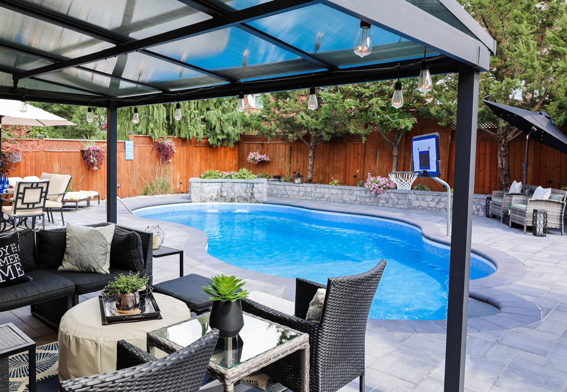 Patio surrounding pool in a residential backyard with an attractive pattern of grey interlocking rectangular pavers of varying sizes and a raised interlocking stone garden in the background.