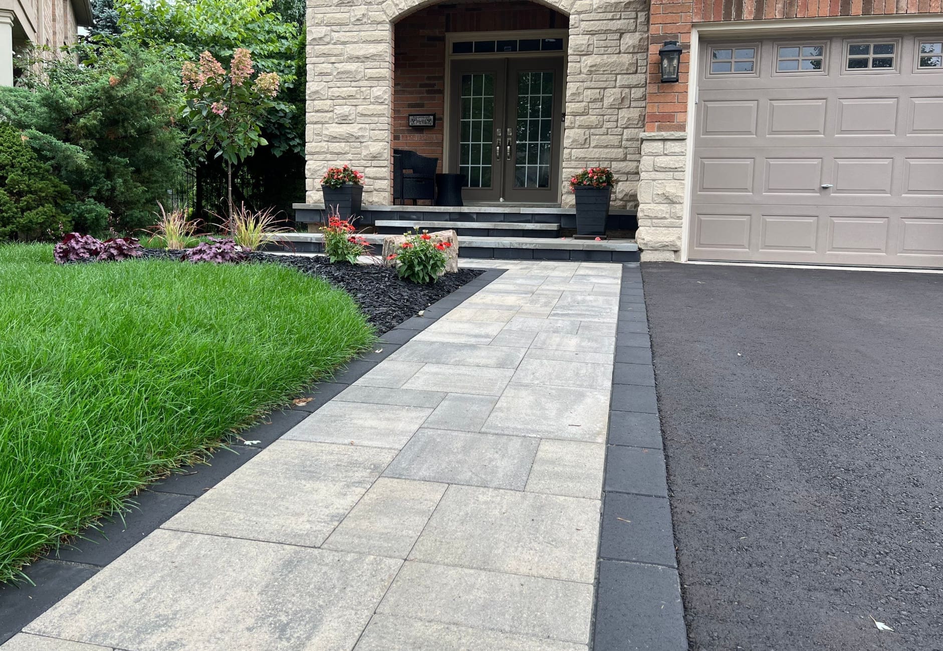 Paver stone walkway consisting of grey rectangular pavers of varying sizes between the front lawn and driveway of a residential property.