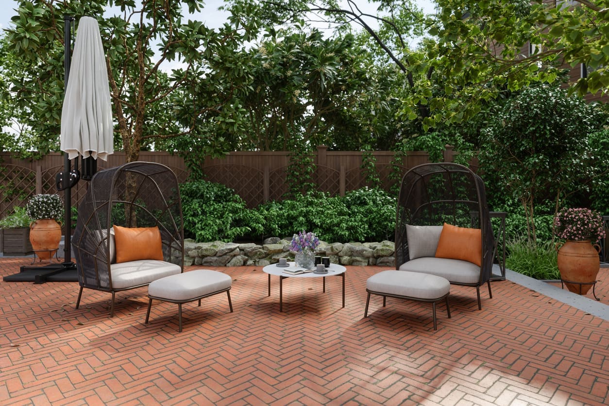 Herringbone-pattern interlocking brick patio with modern outdoor furniture, surrounded by lush greenery and privacy fencing, Showcasing an elegant yet simple landscaping idea.