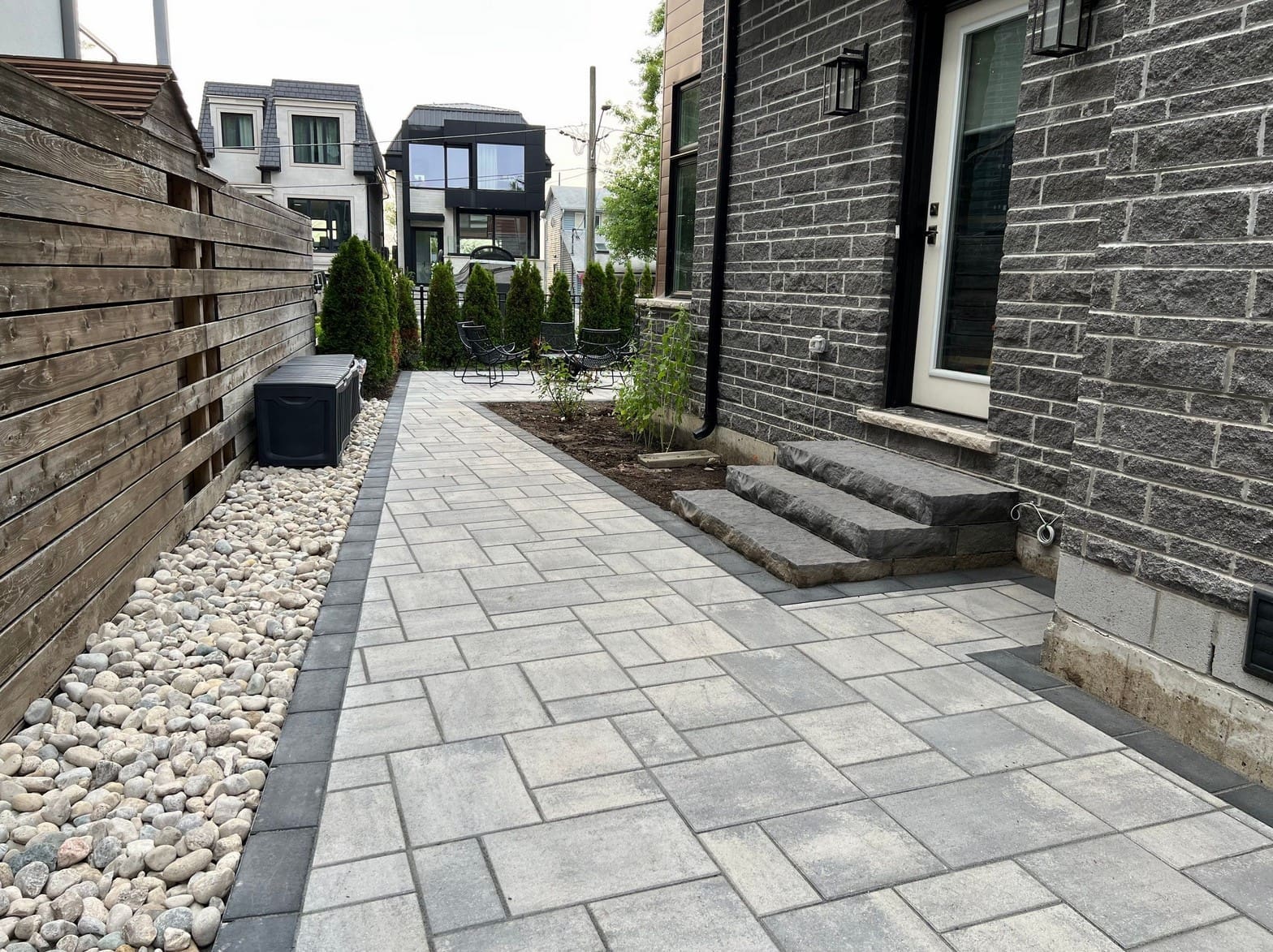 Curved stone walkway laid with interlocking pavers, surrounded by lush greenery and tropical landscaping, illuminated by garden lights at night.