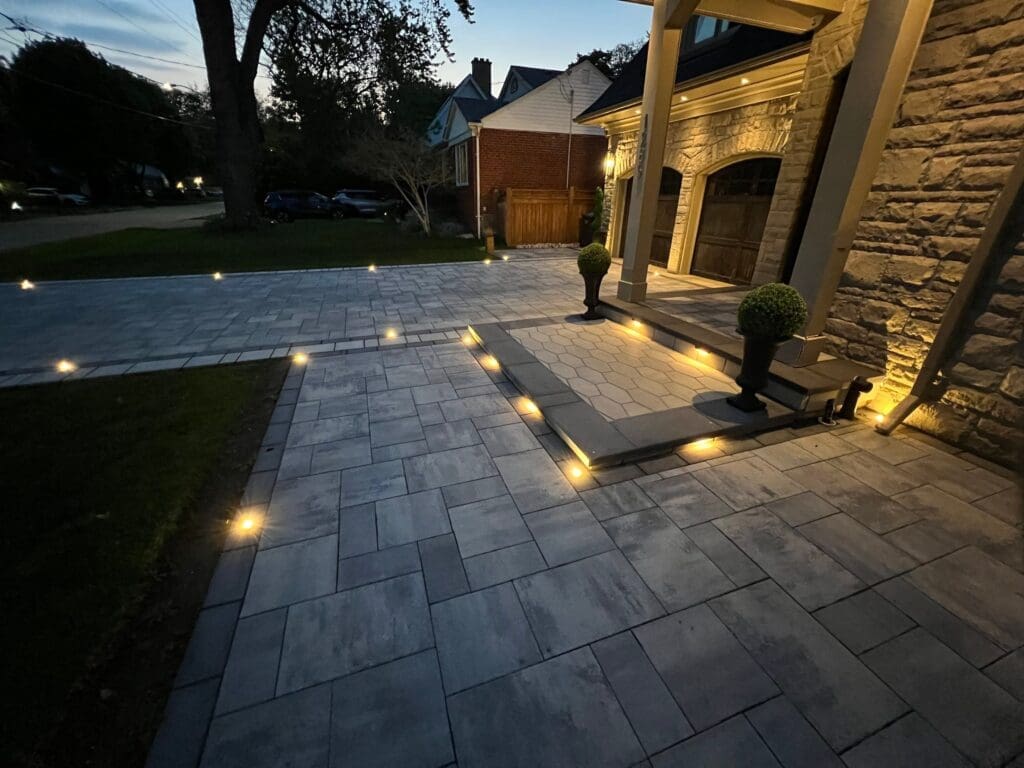 Elegant interlocking driveway and front walkway illuminated with built-in LED landscape lighting at dusk.