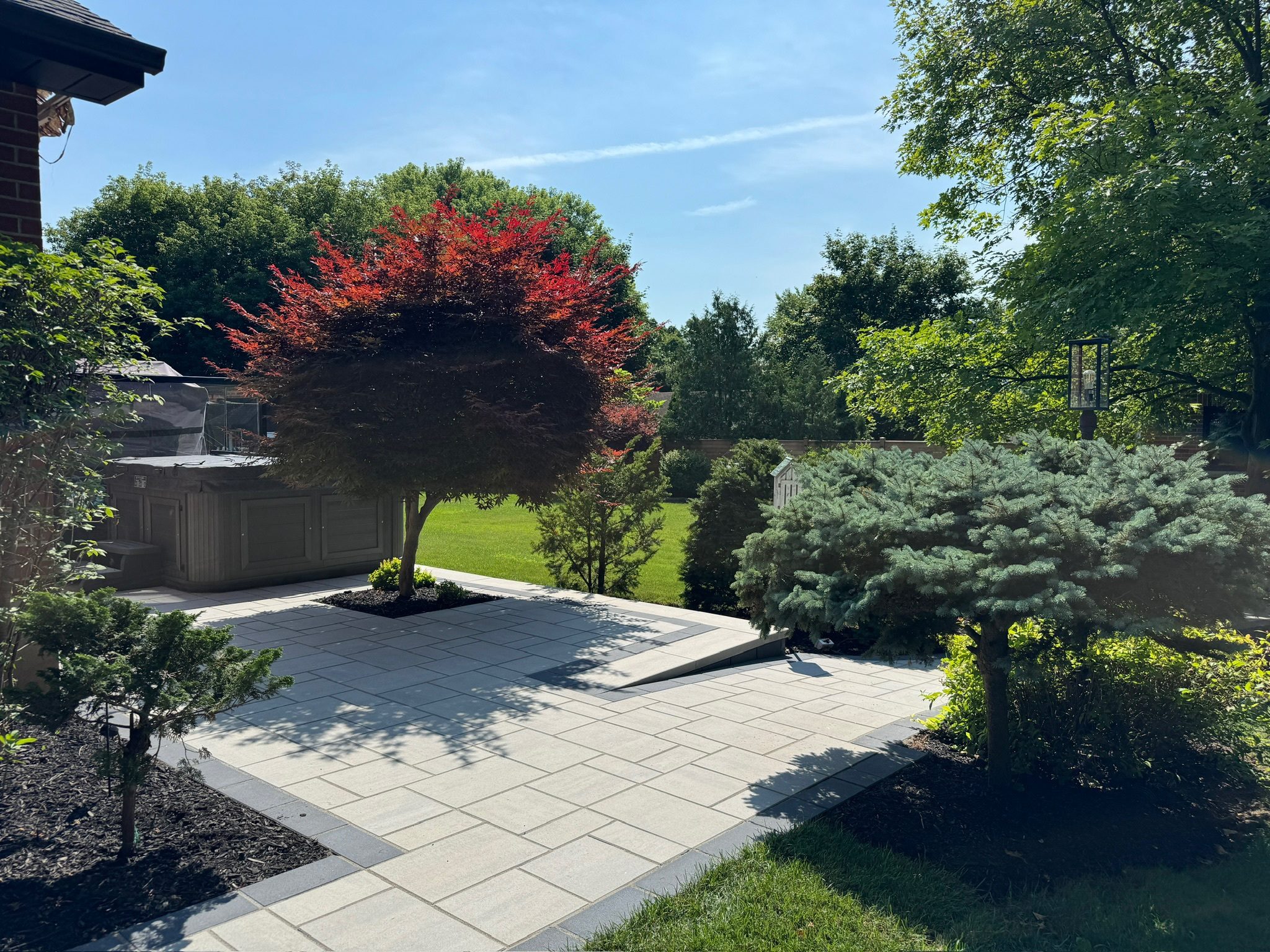 A homeowner spreads black mulch in a well-maintained garden bed in front of a brick house during spring landscaping.