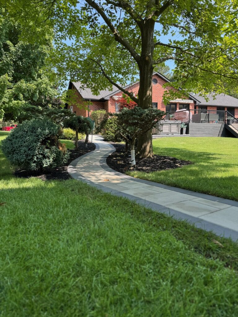 A homeowner spreads black mulch in a well-maintained garden bed in front of a brick house during spring landscaping.