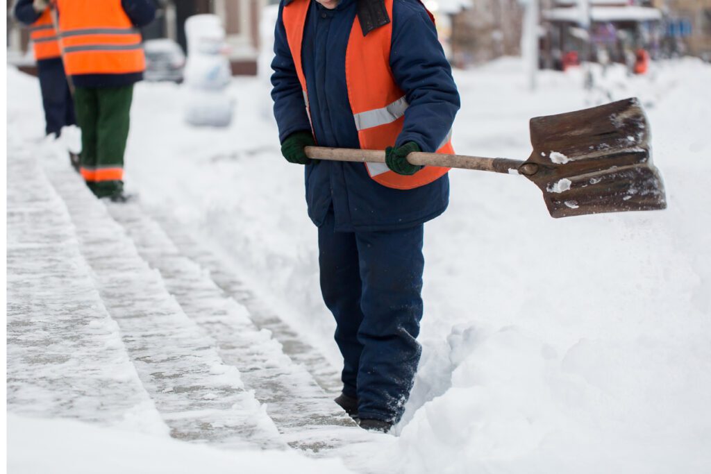 Worker using plastic shovel to clear snow from interlock driveway during Canadian winter.