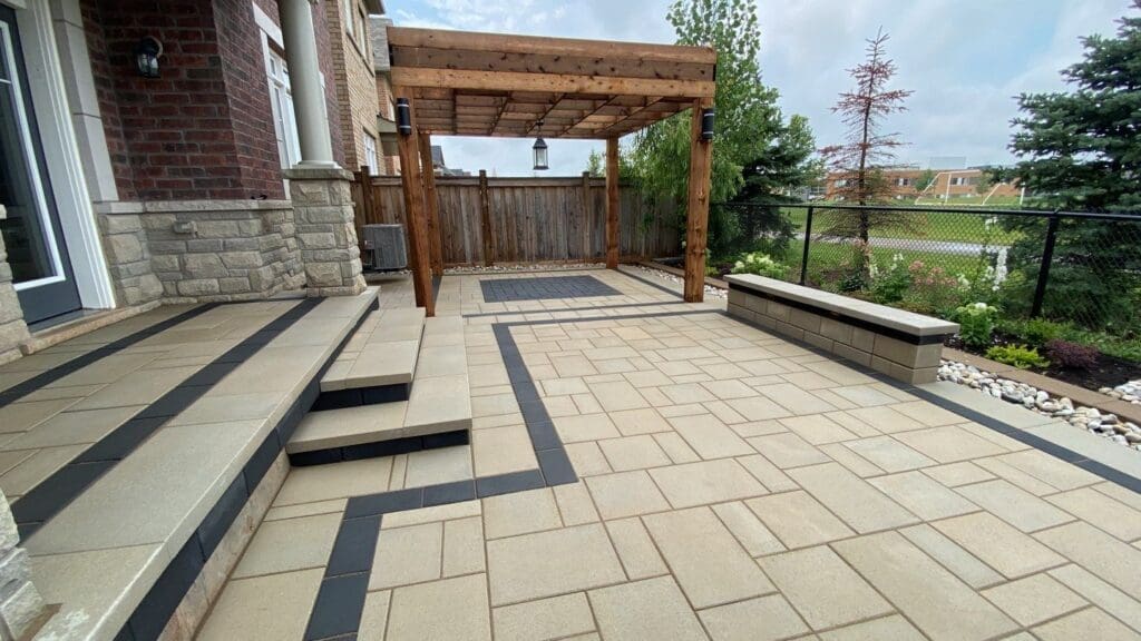 Contemporary interlock backyard patio with beige and charcoal pavers, a wooden pergola, built-in seating and steps leading to a back door with stone veneer.