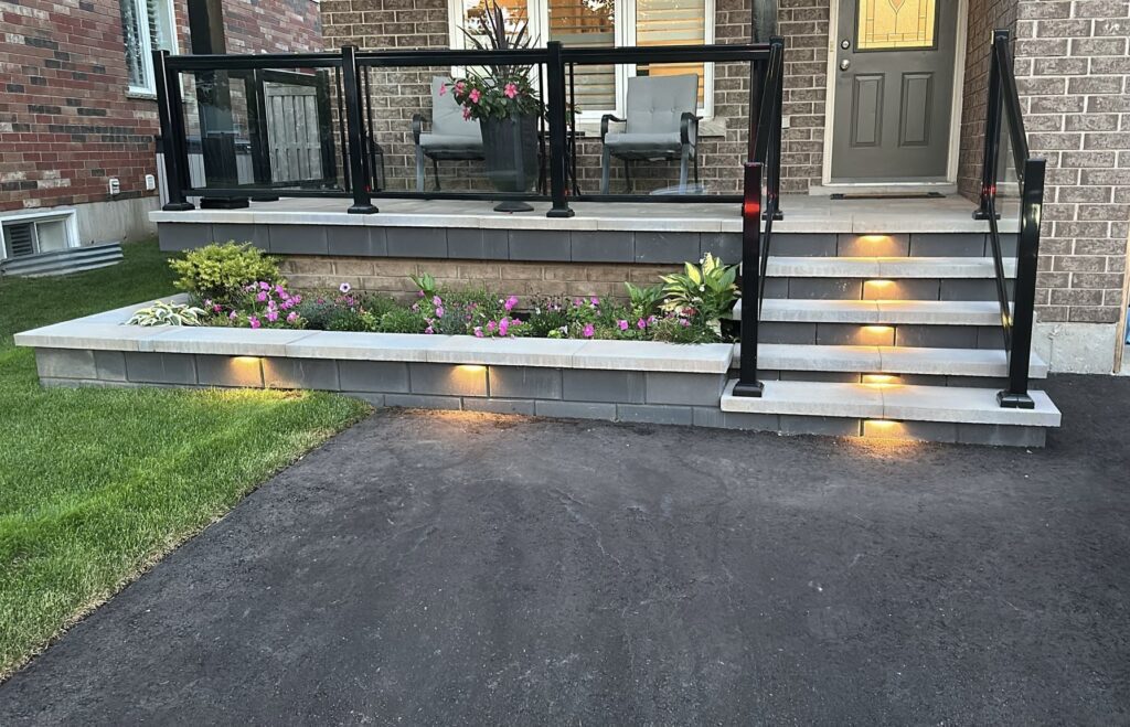 Modern front porch with interlocking stone steps, built-in lighting and a flower bed, showcasing contemporary landscaping and curb appeal.