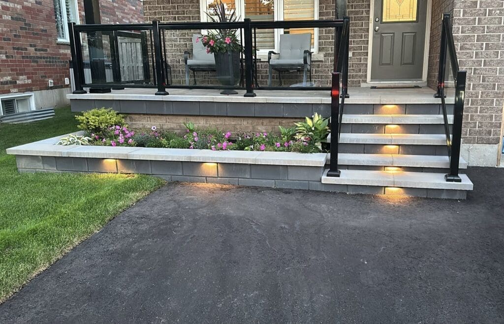 Modern front porch with interlocking stone steps, built-in lighting and a flower bed, showcasing contemporary landscaping and curb appeal.