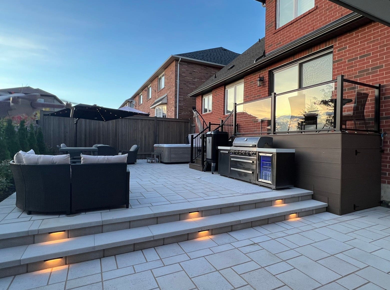 Backyard interlocking patio designed for outdoor living with seating area, steps and built‑in lighting.