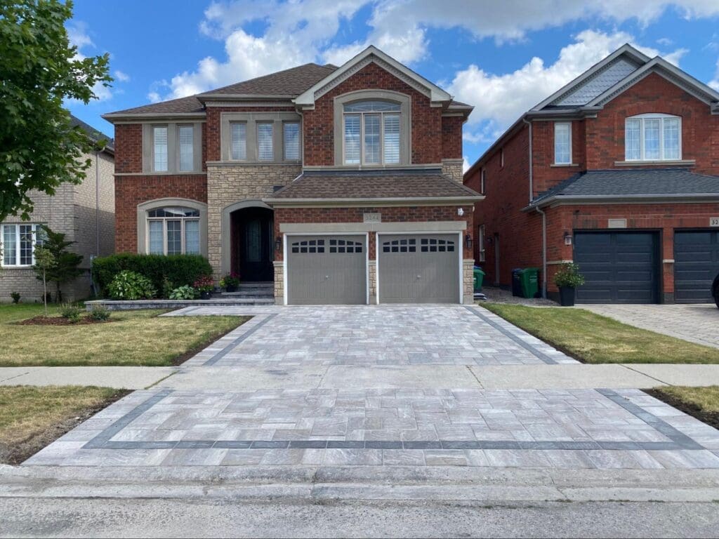 Front view of a modern suburban home with a newly installed interlocking stone driveway and clean landscaping under a blue sky.