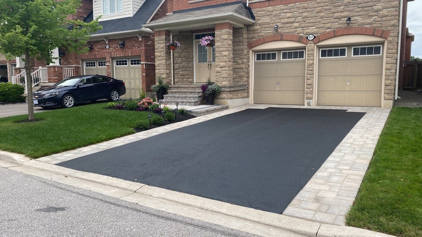 Asphalt driveway framed with interlocking stone borders highlighting a clean, finished driveway design.