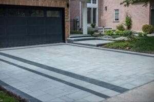Modern interlocking driveway with light grey pavers and dark border accents in front of a suburban home