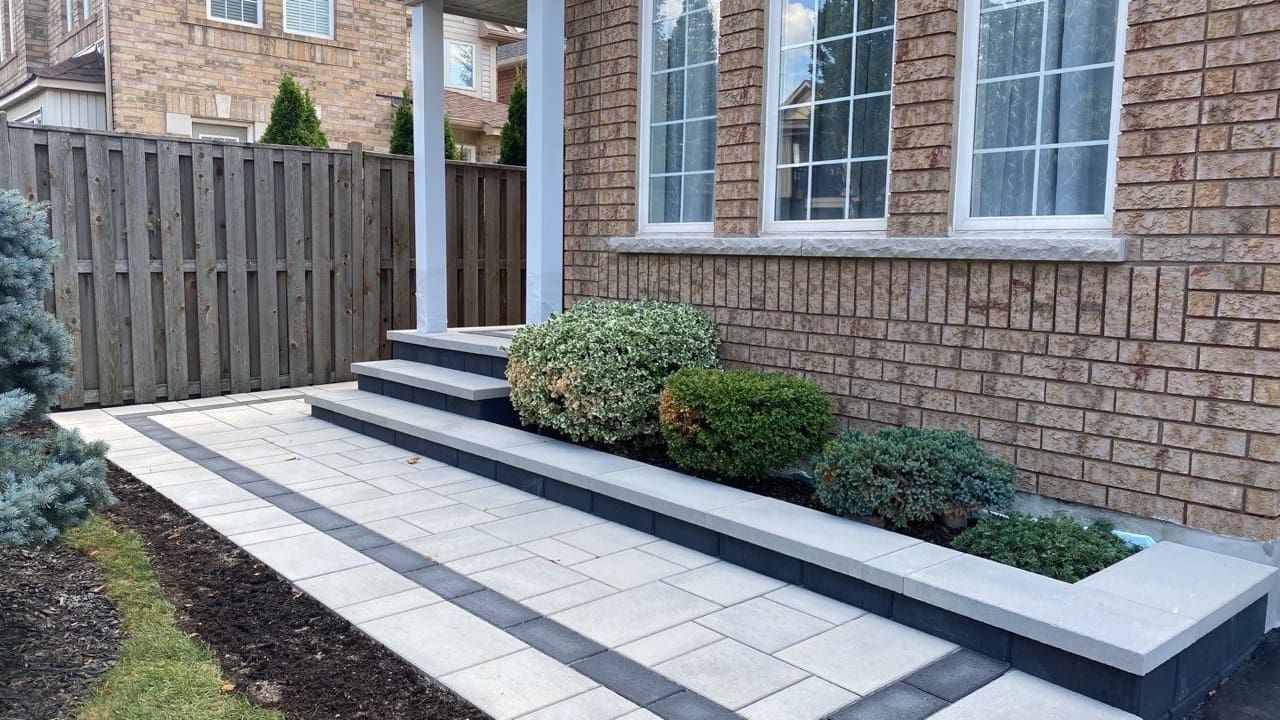 Interlocking Oakville front entrance walkway with charcoal border, natural stone steps and garden beds beside a brick home.
